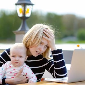 Tired young mother working oh her laptop and holding 6-month daughter