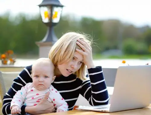 Tired young mother working oh her laptop and holding 6-month daughter