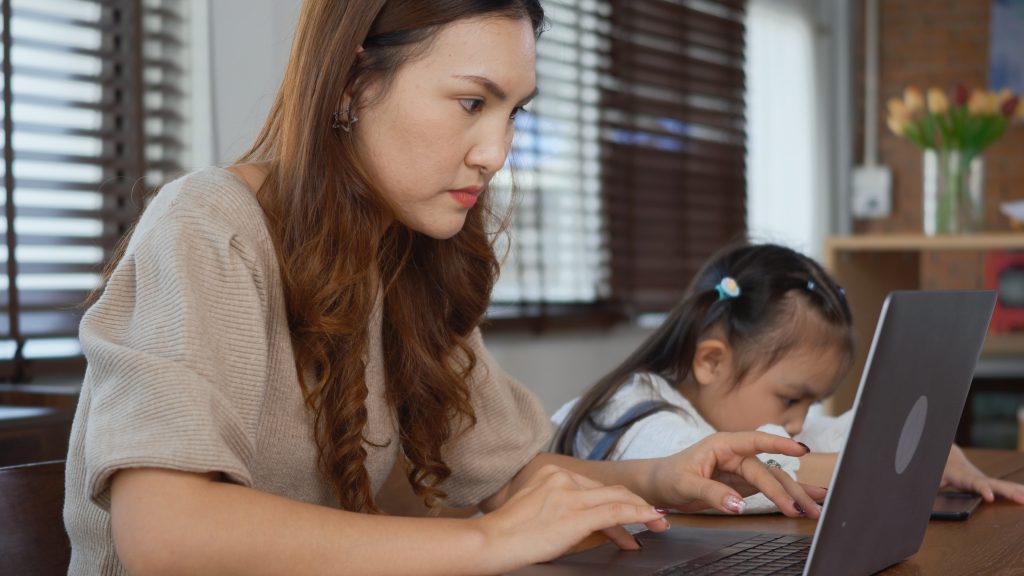 Asian young mother working with laptop computer at home and help daughter doing homework, Single mom freelancer work from home and helping his girl kid teaching homework on desk