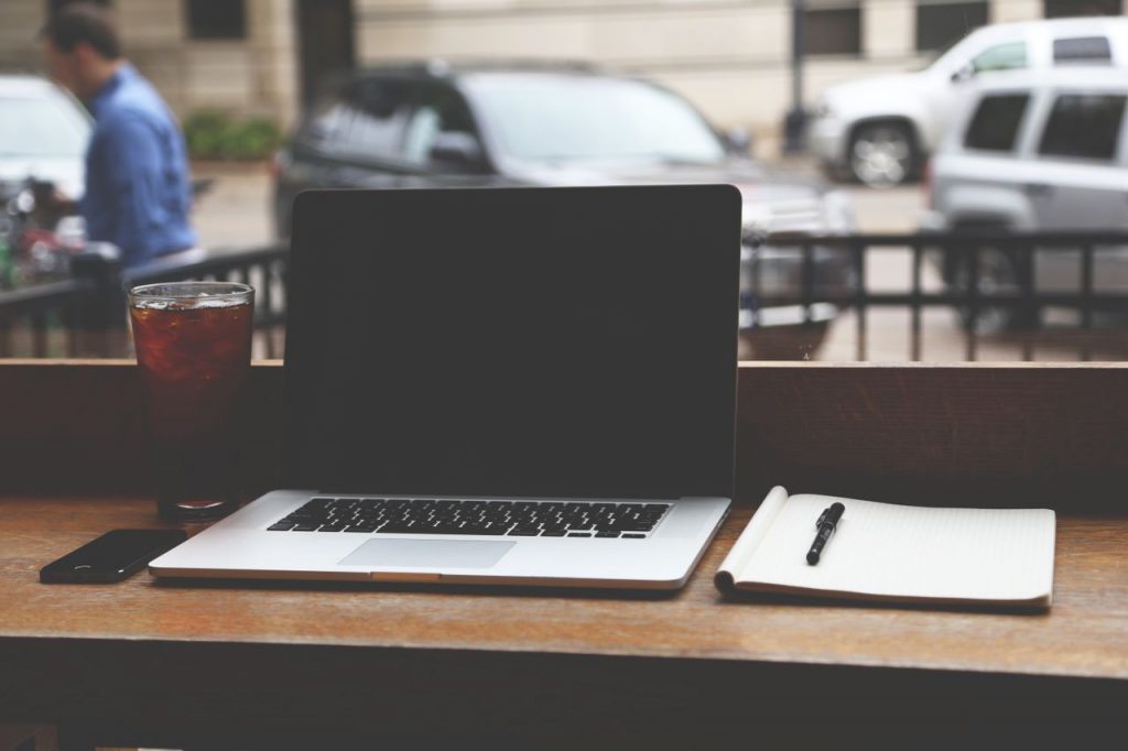 MacBook Pro on a wooden table with iced coffee and notebook in a casual coffee shop setting.